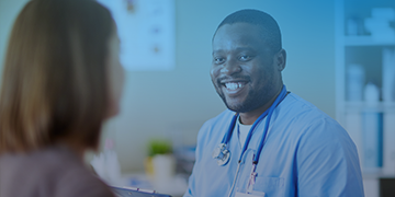 Image shows a male doctor smiling at his female patient who is facing away from the camera.